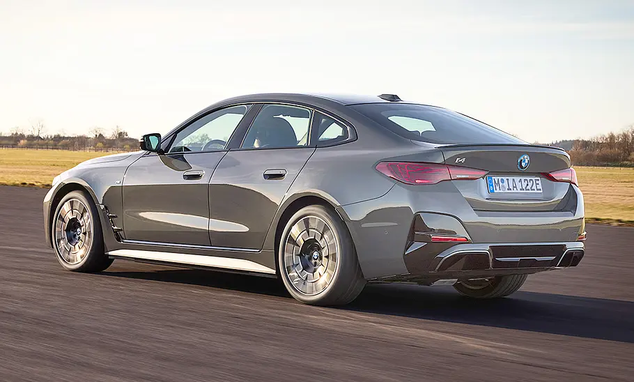 Das BMW i4 Facelift (2024) fährt eine Straße entlang, von hinten links fotografiert.