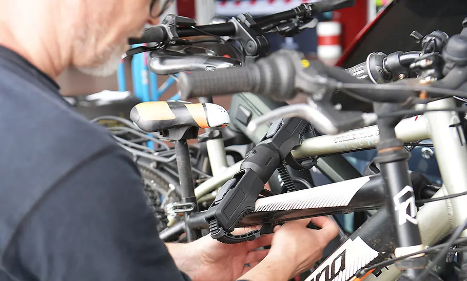 Thule-Fahrradträger für bis zu drei E-Bikes im Test Das Detailfoto zeigt die Hand eines Testers, der die Befestigungsratsche der Rahmenhaltenung am Rahmen eines Testfahrrads zuzieht.