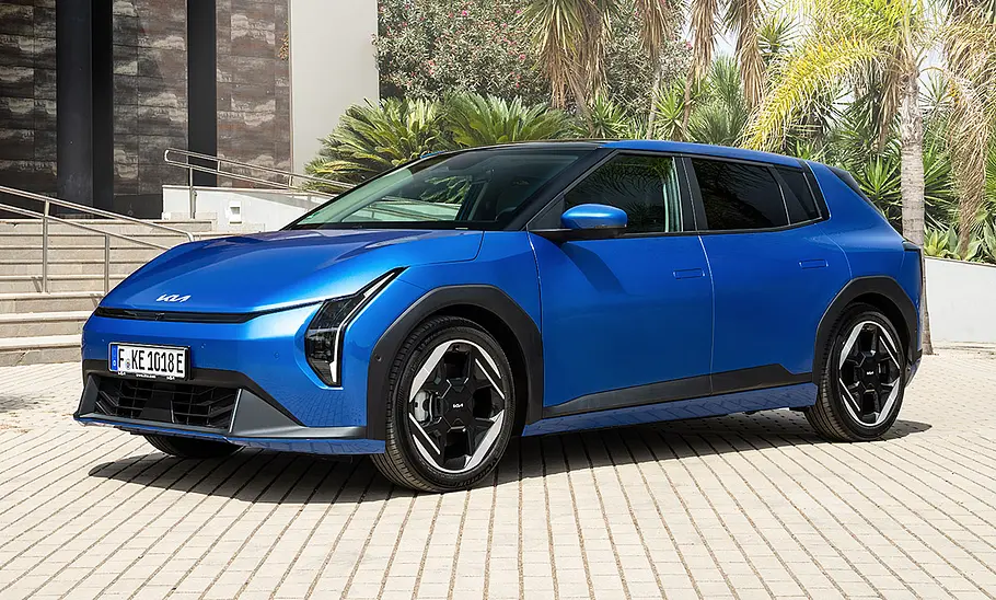 Kia EV4 (2025) Der Kia EV4 (2025) steht auf einem gepflasterten Platz vor einer Außentreppe, von vorne links fotografiert.