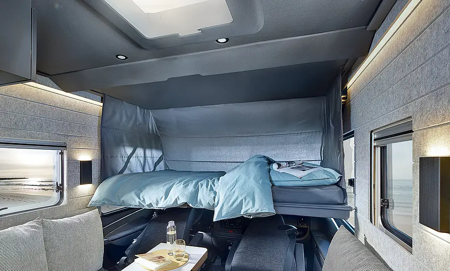 Wohnraum des Niesmann + Bischoff iSmove (2024), Ansicht auf das heruntergeklappte Hubbett in der Fahrerkabine.