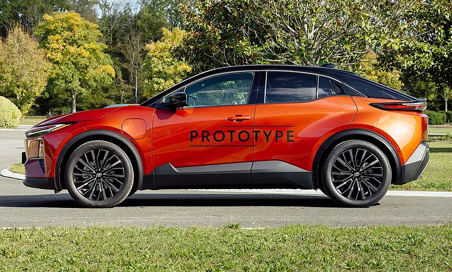 Toyota C-HR+ (2025) Der Toyota C-HR+ (2025) steht auf einer Straße im Grünen, von links fotografiert.