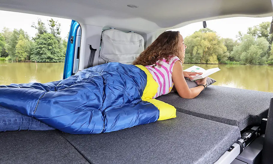 VW Caddy California (2020) Innenraum, Person liegt mit Schlafsack auf ausgeklappter Liegefläche