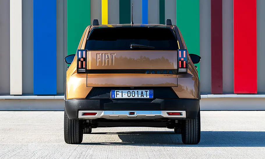 Der Fiat Grande Panda Hybrid (2025) steht vor einer bunt eingefärbten Wand, von hinten fotografiert.