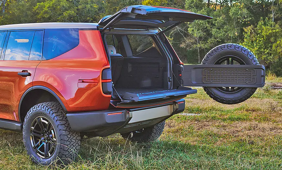 Scout Taveler Concept (2024) stehend auf einer Wiese, Heckklappe geöffnet, Ansicht von links hinten. Die vordere Hälfte des Fahrzeugs ist nicht im Bild.