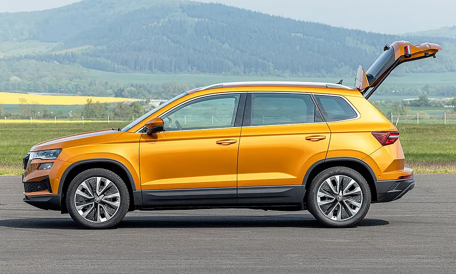 Skoda Karoq (2021) Der Skoda Karoq (2021) steht mit geöffneter Heckklappe vor einer Wiese auf Beton, von links fotografiert.