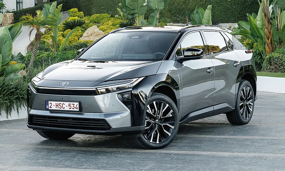 Das Toyota bZ4X Facelift steht vor einem Garten, von vorne links fotografiert.