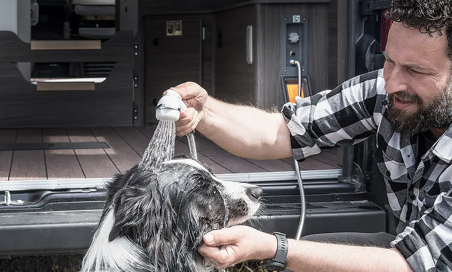 Van Tourer 630 L (2026) Eine Person duscht mit der Außendusche einen Hund hinter dem Van Tourer 630 L (2026).