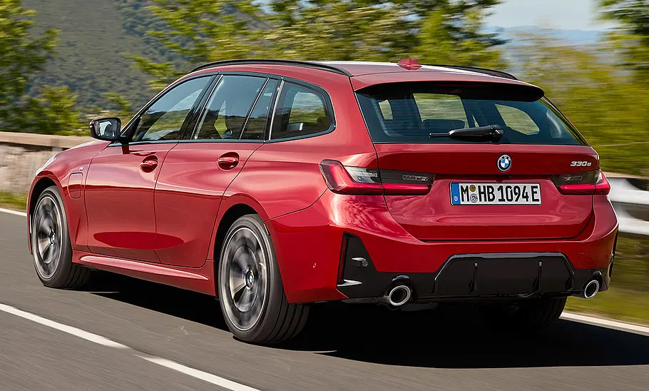 Das BMW 3er Touring Facelift (2024) fährt auf einer Landstraße, von hinten links fotografiert.
