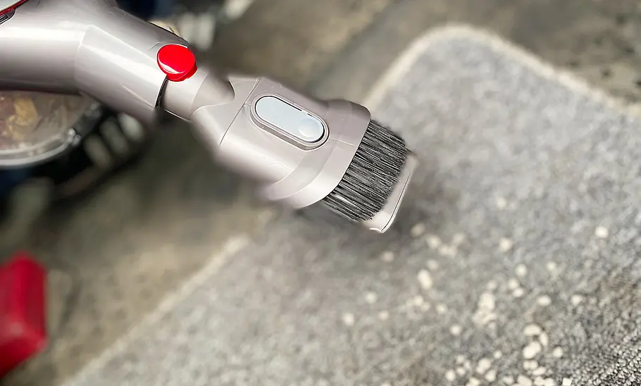 Die Detailaufnahme zeigt den Bürstenkopf des Dyson Akku-Staubsauger Car & Boat V8 beim Absaugen einer Fußmatte mit Katzenstreu darauf.