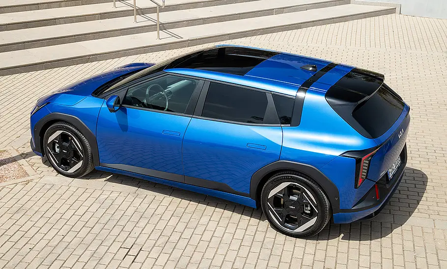 Kia EV4 (2025) Der Kia EV4 (2025) steht auf einem gepflasterten Platz vor einer Außentreppe, obersichtig von hinten links fotografiert.