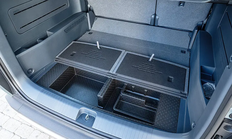 Der Kofferraum des Kia PV5 Passenger (2025) mit aufgeklappten Fächern unter dem Ladeboden.
