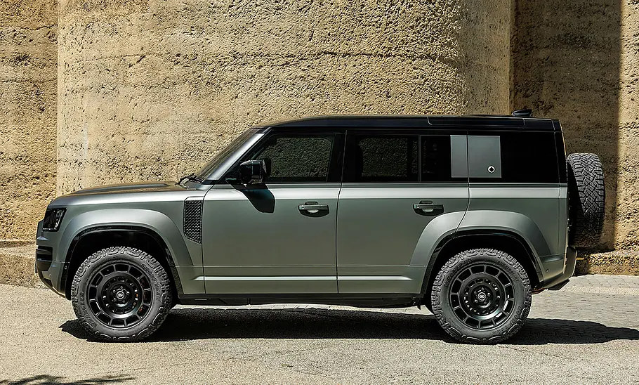 Land Rover Defender Octa (2024) steht vor einer Sandstein-Wand, Ansicht von links.