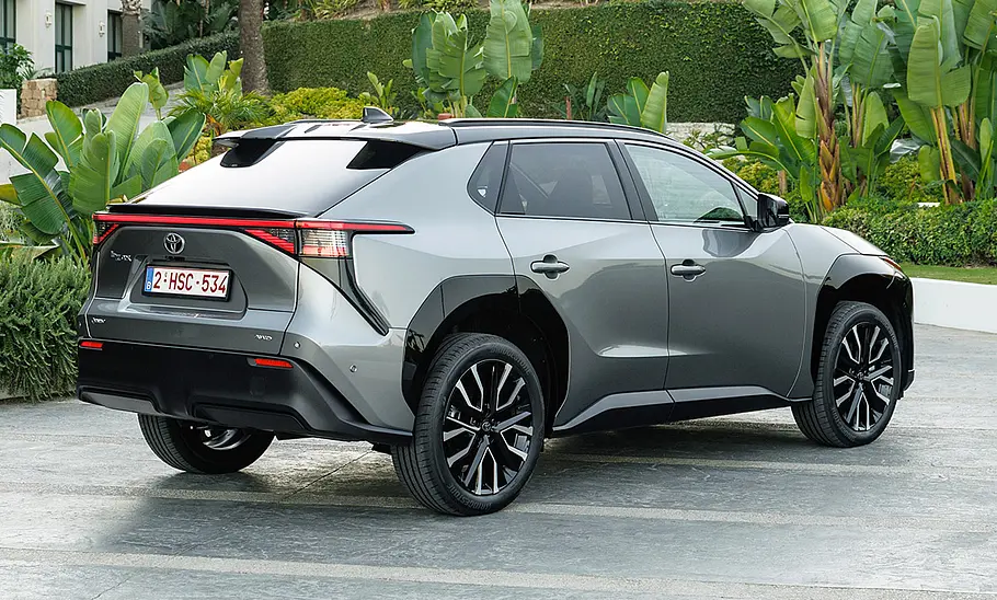Das Toyota bZ4X Facelift steht vor einem Garten, von hinten rechts fotografiert.