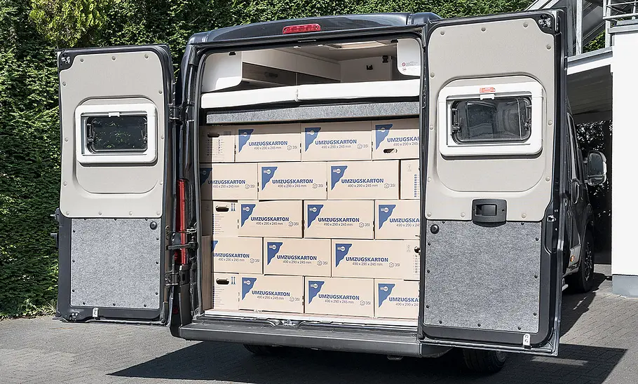 Van Tourer 630 L (2026) Die Hecktüren des Van Tourer 630 L (2026) sind geöffnet und geben den Blick frei auf den mit Umzugskartons vollgeräumten Camper. Das optionale Hubbett ist dazu ganz nach oben gefahren.