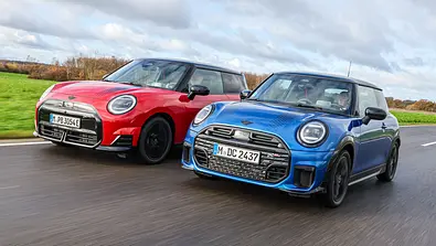 Die beiden Mini Cooper fahren nebeneinander auf einer Landstraße und wurden von vorne schräg fotografiert. - Foto: Daniela Loof