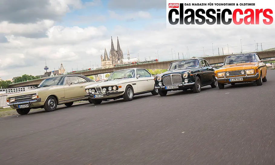 Die Autos Opel Commodore A Coupé, BMW 2800 CS, Rover P5B Coupé & Ford 20M RS Coupé fahren an einer Straße am Rhein entlang, fotografiert von vorne schräg.
