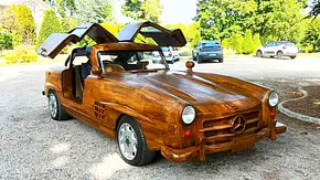 Der Mercedes Benz 300 SL aus Holz steht auf einem Parkplatz und wurde von vorne schräg fotografiert. - Foto: Rouillac Auktionshaus