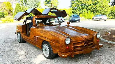 Der Mercedes Benz 300 SL aus Holz steht auf einem Parkplatz und wurde von vorne schräg fotografiert. - Foto: Rouillac Auktionshaus