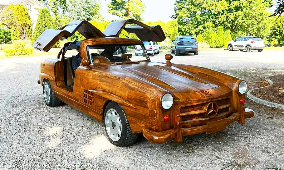 Mercedes Benz 300 SL aus Holz Der Mercedes Benz 300 SL aus Holz steht auf einem Parkplatz und wurde von vorne schräg fotografiert.