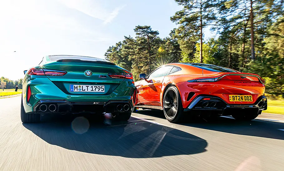 Der BMW M8 Competition & der Aston Martin Vantage V8 fahren nebeneinander auf der Rennstrecke her. Blick von hinten.