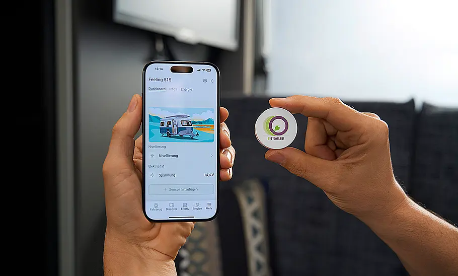 Das Bild zeigt die Smartphone-Steuerung per Eriba-App im Eriba Novaline (2025). Im Foto hält eine Person ein Smartphone sowie einen Button mit der Aufschrift E-Trailer.