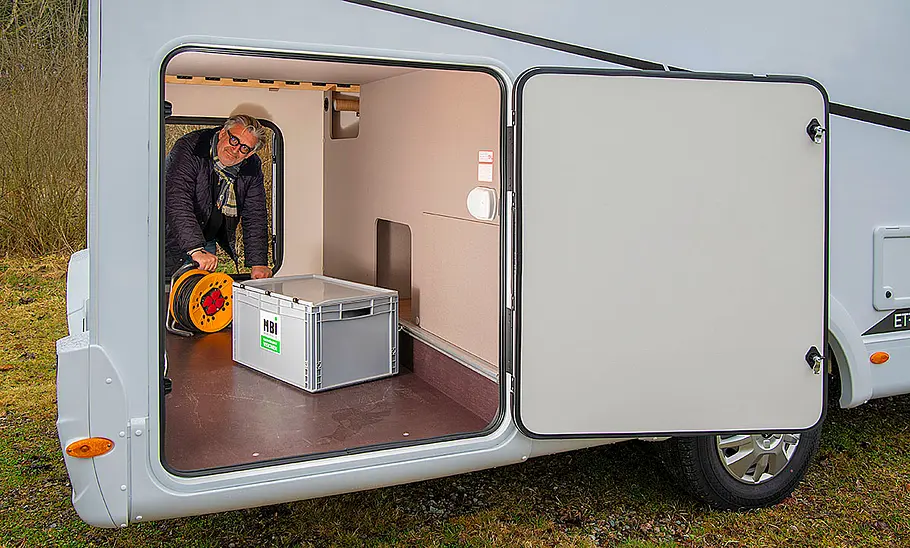 Das Bild zeigt die Heckgarage des Etrusco T 6.9 SB (2025) durch die geöffnete rechte Garagentüre fotografiert. Eine Person lädt von der linken Seite Gepäck ein.
