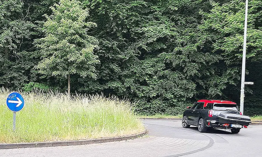 Thule-Fahrradträger für bis zu drei E-Bikes im Test Die Außenaufnahme zeigt den mit einer Heckbox an der Anhängerkupplung eines Mini Cooper montierten Fahrradträger Thule Easyfold 3, der in einem Kreisverkehr nach rechts zur Seite ruscht.