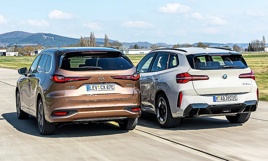Blick von schräg hinten auf die beiden fahrenden SUV Mazda CX-80 und BMW X3.