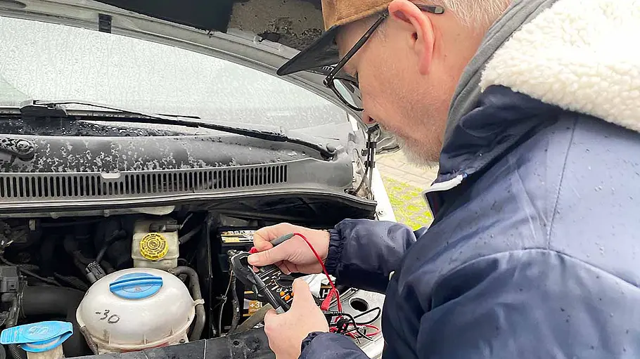 Starthilfe-Powerbanks im Test Ein Tester misst mit einem speziellen Gerät die Spannung der Starterbatterie eines Autos.