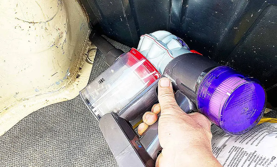 Das Foto zeigt die Fugendüse des Dyson Akku-Staubsaugers Car & Boat V8 beim Aufsaugen von Katzenstreu im Kofferraum eines älteren Autos.