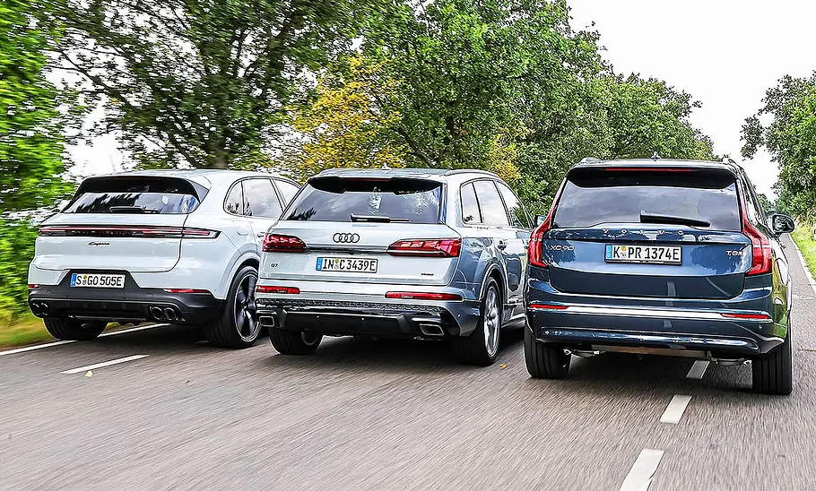 Blick von hinten auf die drei SUV Porsche Cayenne, Audi Q7 und Volvo XC90, die in Formation nebeneinander herfahren.
