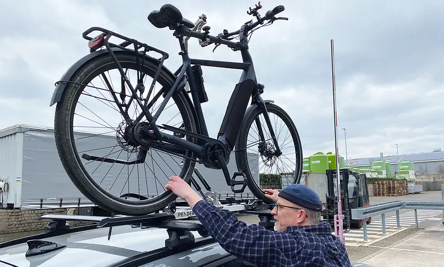 Test-Redakteur justiert ein E-Bike auf dem Autodach mit Pender Ebikelifter.