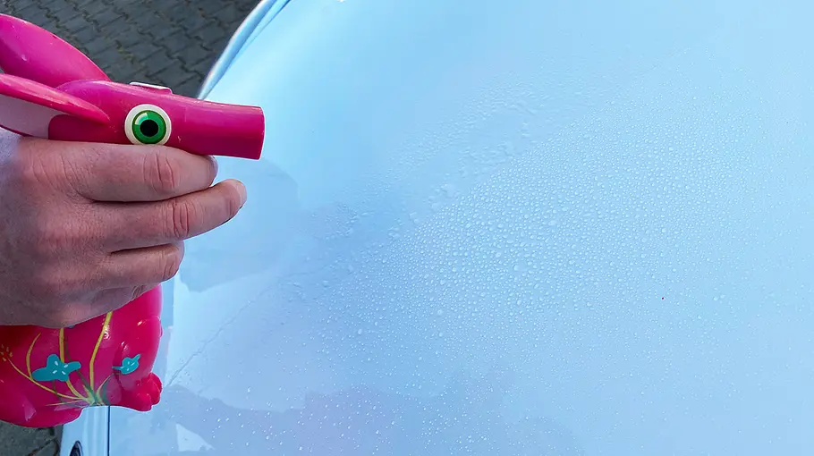 Wassersprühpistole beim Benetzen einer Motorhaube, Abperleffekt des Wassers ist zu sehen.