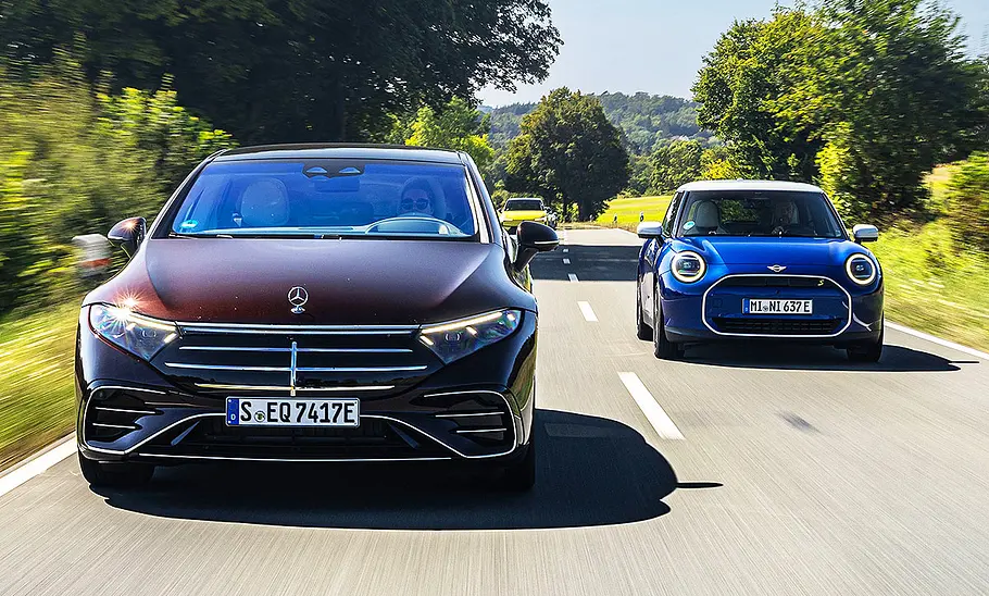 Der Mercedes EQS und der Mini Cooper SE auf der Landstraße, von schräg vorne fotografiert.
