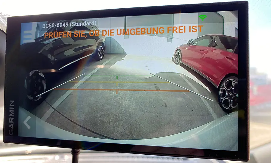 Garmin DriveSmart 66 MT-S im Rückfahrmodus mit zwei anderen Autos, fotografiert an der Windschutzscheibe eines Autos.