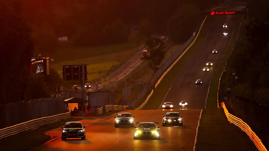 Blick auf die Döttinger Höhe vom Nürburgring mit vielen Rennautos auf der Rennstrecke bei Sonnenuntergang.