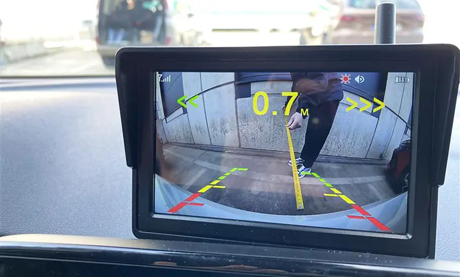 Tester beim Messen der Distanz zwischen Auto und Mauer, aufgenommen durch eine Rückfahrkamera.