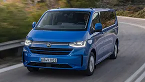Der VW e-Caravelle fährt auf einer Straße. Ansicht des Fahrzeugs von vorne links. - Foto: VW Nutzfahrzeuge