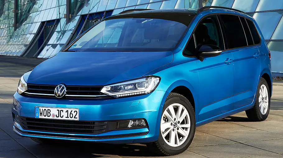 VW Touran Der VW Touran steht vor einer Glasfassade, von vorne links fotografiert.