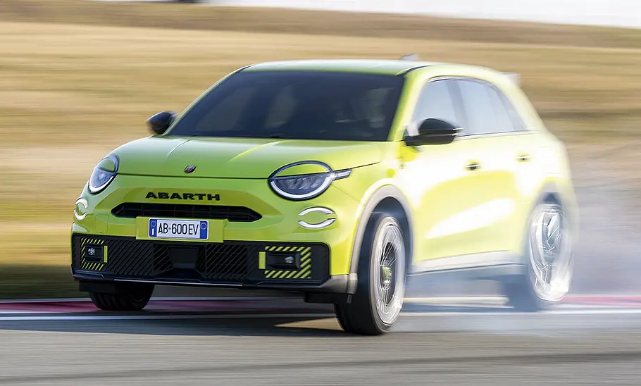 Der Abarth 600e (2024) driftet durch eine Kurve, von schräg vorne fotografiert.