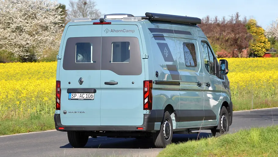 Der Ahorn Camp CV 560 fahrend von schräg hinten rechts auf einer Landstraße zwischen blühenden Rapsfeldern.