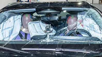 Der Innenraum des Audi A5 (2024) ist nach einem Euro NCAP-Crashtest durch die gesprungene Windschutzscheibe fotografiert. Zwei Dummies sitzen inmitten mehrere offener Airbags. - Foto: Euro NCAP