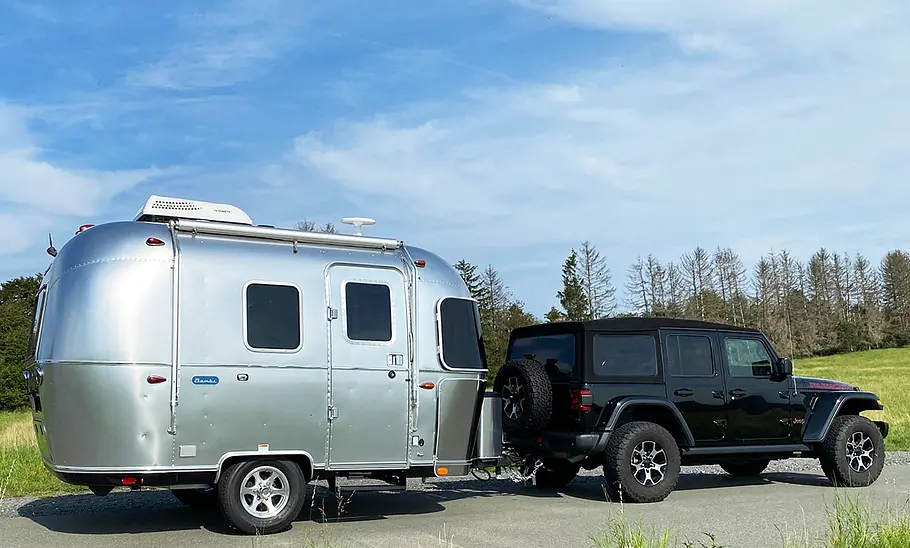 Die Außenaufnahme zeigt den Airstream Bambi 16 (2025) von schräg seitlich am Hänger eines Jeeps als Zugfahrzeug.