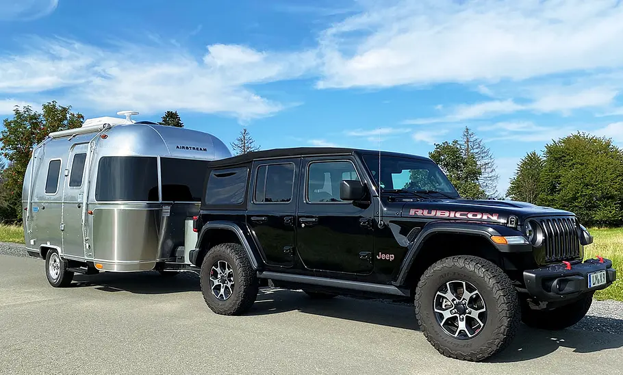 Die Außenaufnahme zeigt den Airstream Bambi 16 (2025) von schräg vonre am Hänger eines Jeeps als Zugfahrzeug.