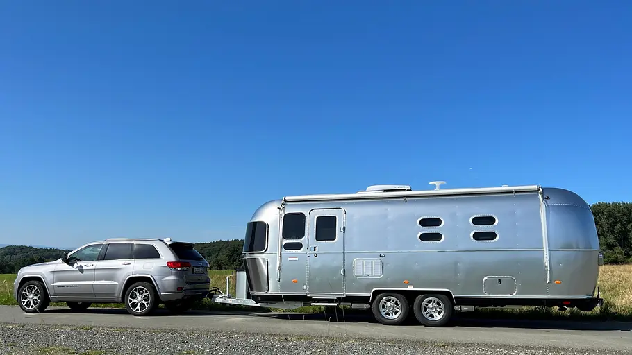 Airstream International 25 IB (2025) Die Außenaufnahme zeigt den Airstream International 25 IB am Haken eines Geländewagens als Zugfahrzeug.