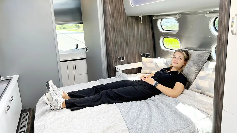 Airstream International 25 IB (2025) Die Innenaufnahme zeigt eine junge Frau, die auf dem Bett des Airstream International 25 IB (2025) liegt.