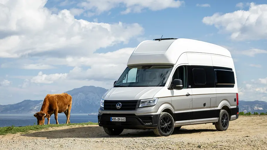 Der VW Grand California statisch von schräg vorne links auf dem Punta Camorro mit Blick in Richtung Marokko (im Hintergrund). Neben dem Van grast eine Kuh.