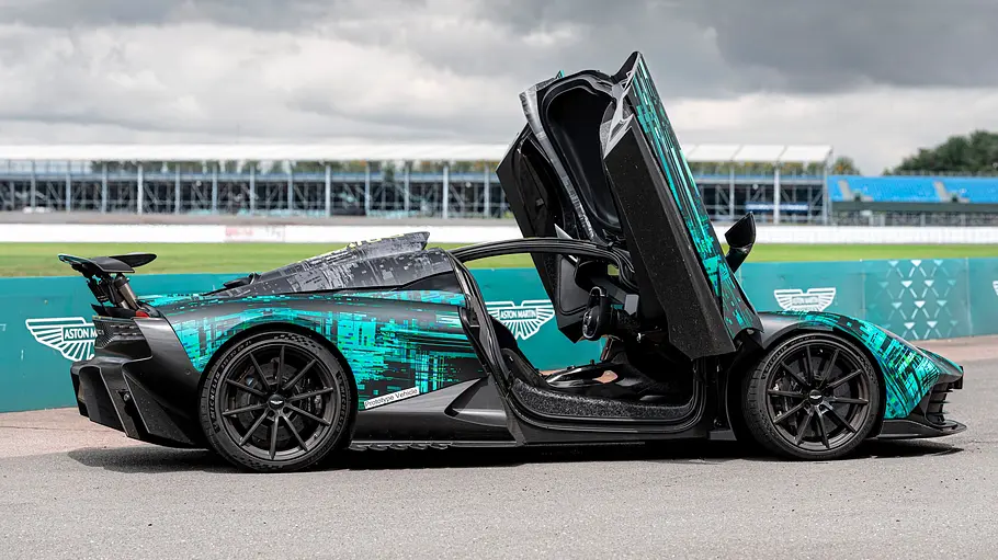 Aston Martin Valhalla steht an der Rennstrecke, Ansicht von der rechten Seite, die Scherentüren sind geöffnet.