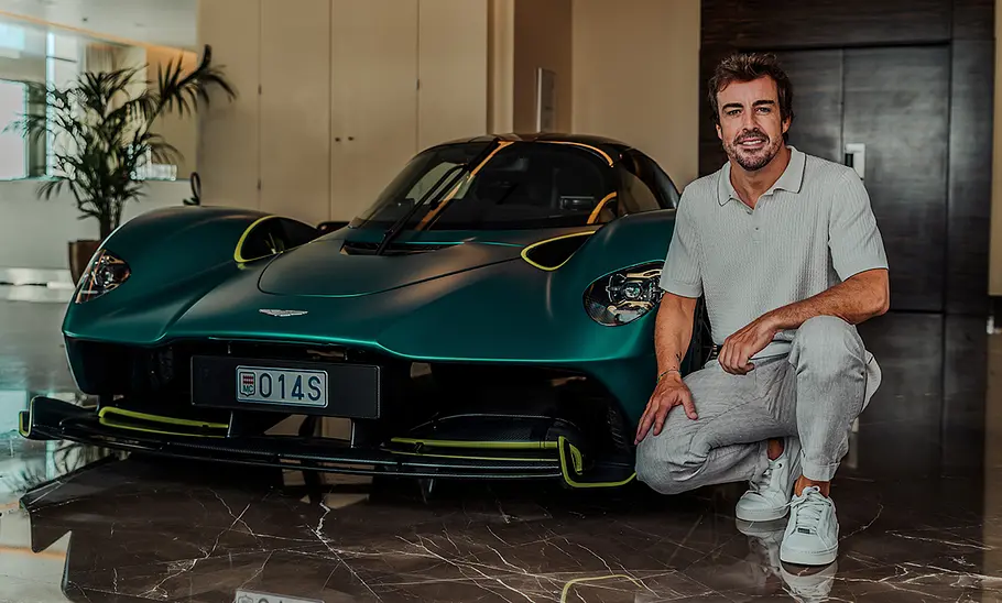 Rennfahrer Fernando Alonso kniend vor seinem Aston Martin Valkyrie.
