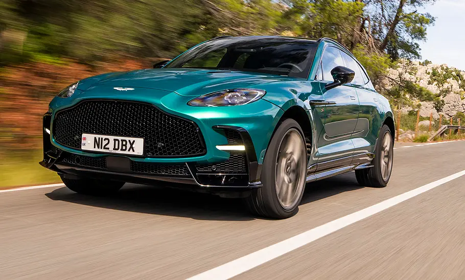 Der Aston Martin DBX S (2025) fahrend auf einer Straße von schräg vorne.